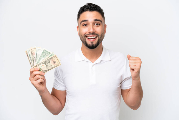 Young Arab man taking a lot of money isolated on white background celebrating a victory in winner position - Zdjęcie, obraz