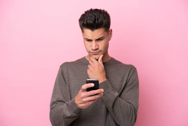 Νεαρός καυκάσιος άνδρας απομονωμένος σε ροζ φόντο σκέφτεται και στέλνει ένα μήνυμα - Φωτογραφία, εικόνα