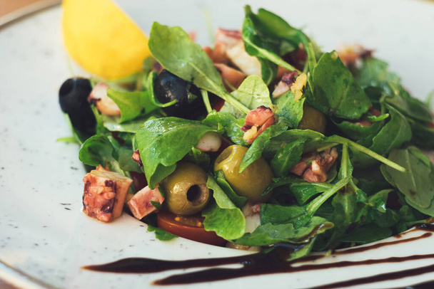 Delicious and light Mediterranean dinner - vegetable octopus salad with olives, capers, leaves and herbs - Photo, Image