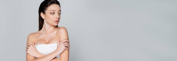 pretty young woman with bare shoulders and makeup looking away isolated on grey, banner - Фото, изображение