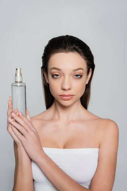 young woman with bare shoulders holding bottle with thermal water isolated on grey - Foto, afbeelding