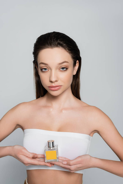 young woman with bare shoulders holding bottle with perfume isolated on grey - Fotografie, Obrázek