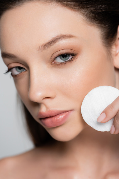 close up view of young woman removing makeup with cotton pad isolated on grey - Photo, image