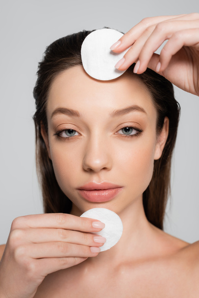 close up view of young woman removing makeup with cotton pads isolated on grey - Photo, Image