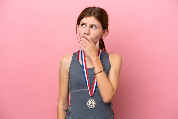 Young English woman with medals isolated on pink background having doubts and with confuse face expression - Foto, Imagen