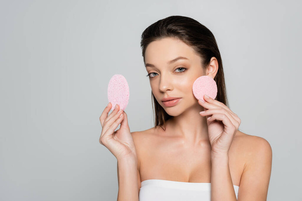 young woman with bare shoulders holding exfoliating sponges isolated on grey - Foto, Bild