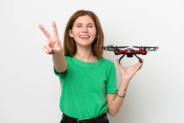 Young English woman holding a drone isolated on white background smiling and showing victory sign - Φωτογραφία, εικόνα