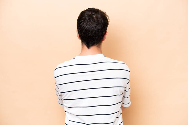 Young caucasian man isolated on beige background in back position - 写真・画像
