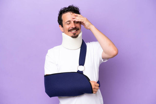 Young caucasian man wearing a sling and neck brace isolated on purple background smiling a lot - Photo, Image
