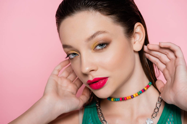 young brunette model with bright makeup posing while looking at camera isolated on pink  - Zdjęcie, obraz