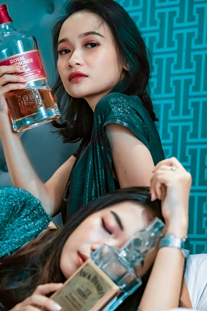 Asian women holding an alcohol bottle in their hand in the bedroom while wearing blue dresses - Fotoğraf, Görsel