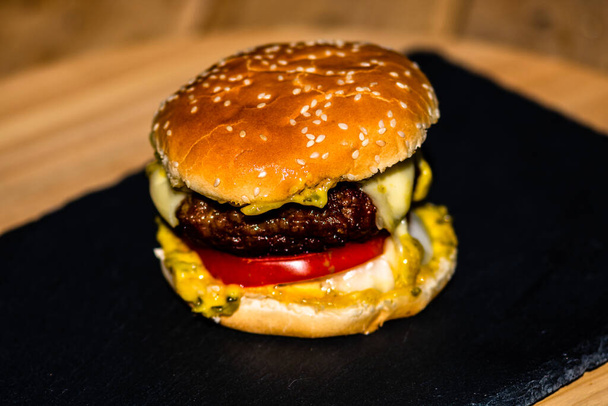Detail of fresh tasty beef cheeseburger with melted cheese isolated on black background - Foto, Imagen