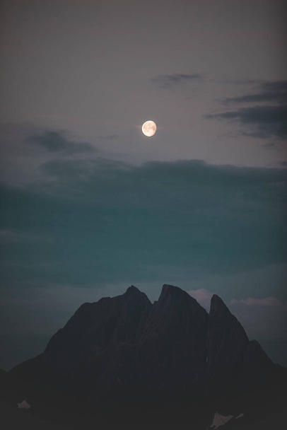 A vertical shot of rocky mount silhouette at night under a full moon sky - Fotó, kép