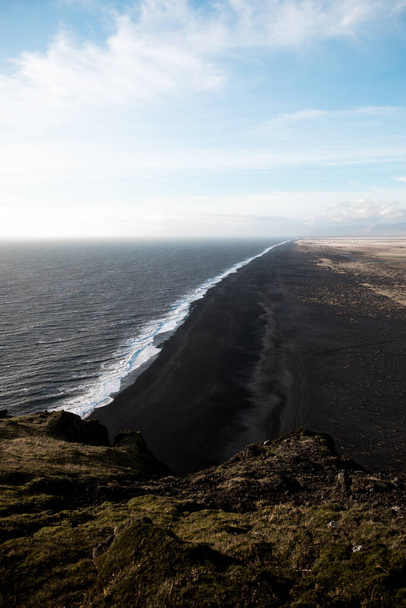 A scenic view of the kirkjufjara beach against blue cloudy sky in bright sunlight in south Iceland - Foto, afbeelding