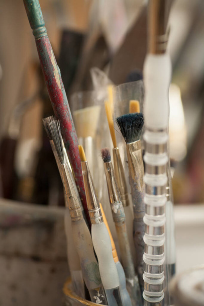 A vertical shot of used paintbrushes and pencils on a blurred background - 写真・画像