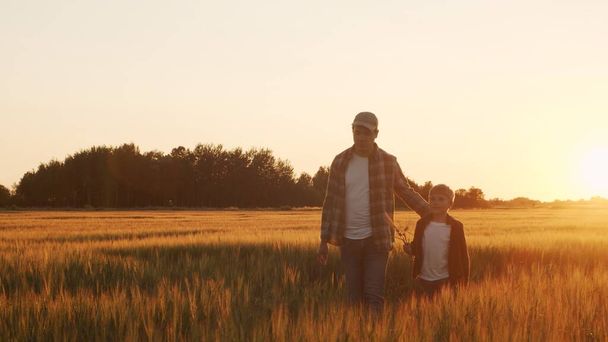 Farmer and his son in front of a sunset agricultural landscape. Man and a boy in a countryside field. The concept of fatherhood, country life, farming and country lifestyle. - Photo, Image