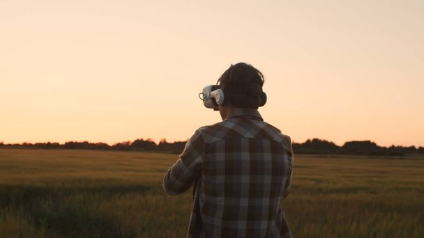 Farmer in virtual reality helmet in front of a sunset agricultural landscape. Man in a countryside field. The concept of country life, food production, farming and technology. - Photo, Image