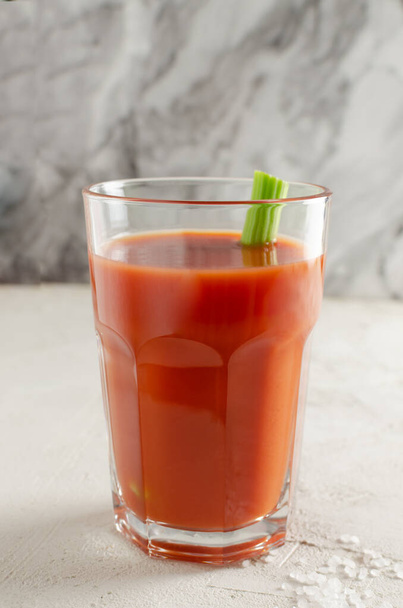 One transparent glass cup with red tomato juice and a sprig of celery on a light background. Healthy food concept. Vertical orientation. Selective focus. - Фото, зображення