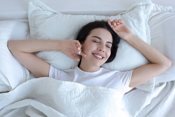 Top view, young beautiful brunette woman sleeping in bed with eyes closed, smiling in sleep wearing white t-shirt pajamas - Photo, image