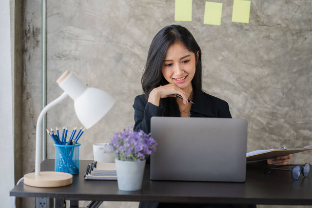 Happy Asian businesswoman using laptop computer while doing financial work. Successful with financial documents on the table - 写真・画像