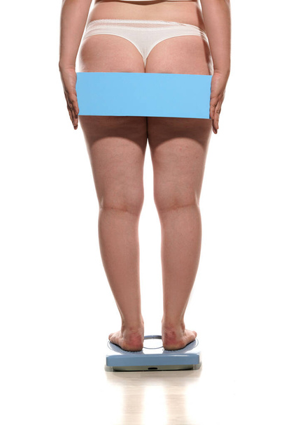 Back view of  obese woman standing on a scale and holding empty board behind her - Photo, Image