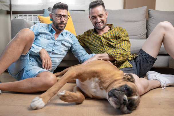 Happy gay couple sitting on floor and playing with dog at home. High quality photography - Foto, immagini