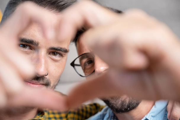 Young gay couple smiling confident doing heart symbol with hands at home. High quality photography. - 写真・画像