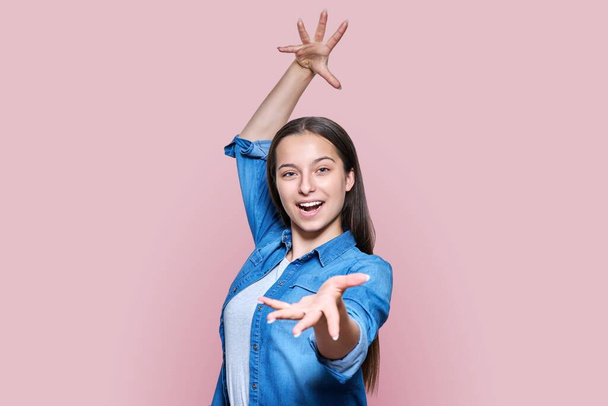 Emotional beautiful teenage girl in expression with arms raised open smile screaming wow, on light pink color studio background. Emotions expression joy happiness success dance concept - Valokuva, kuva