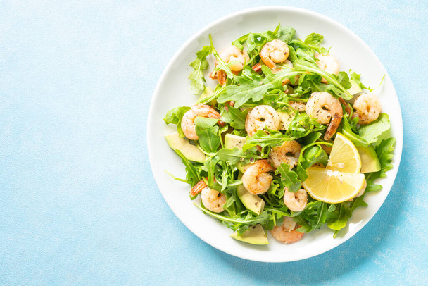 Shrimp salad with arugula and avocado at blue table. Top view with space for text. - Фото, изображение