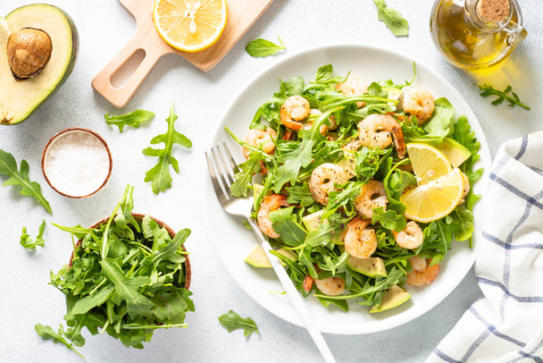 Green shrimp salad with arugula and avocado at white table. Top view image. - Fotó, kép