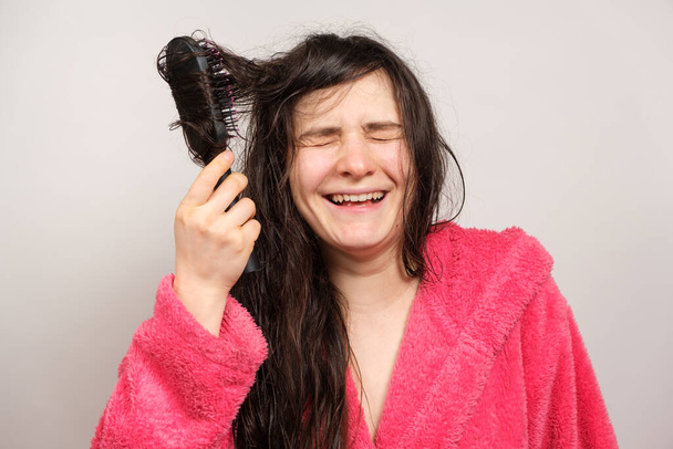 Une femme en robe rose peigne ses cheveux mouillés avec un peigne et rit. - Photo, image