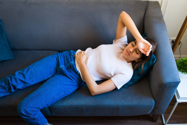 Sick latin woman with one arm on her forehead suffering from a bad headache and resting on the sofa - Foto, Imagem
