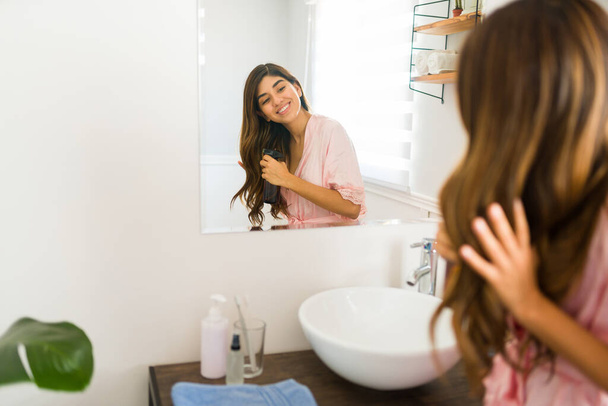 Rear view of a cheerful hispanic woman looking happy while putting hair products on her beautiful shiny hair - Zdjęcie, obraz