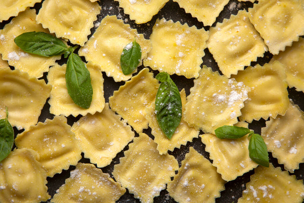Delicious raw ravioli with flour and basil on dark background. The process of making Italian ravioli. Landscape with copy space. - Foto, imagen