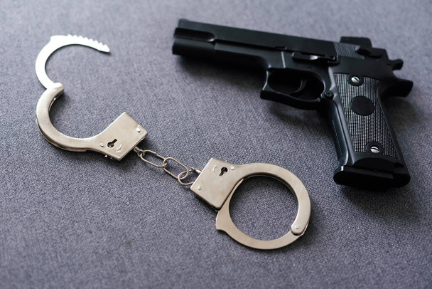 Black gun and metal handcuffs lie on the black background. Private detective work. Searching information. Crime and robbery, prison concept - Photo, Image