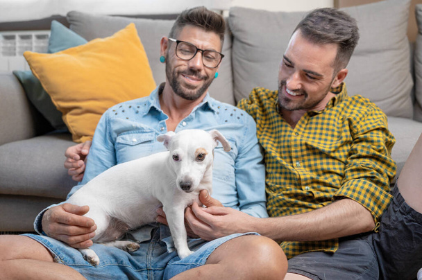Щаслива гомосексуальна пара сидить на підлозі і грає з собакою вдома. Високоякісна фотографія
 - Фото, зображення