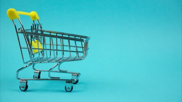 Shopping trolley with books moving on blue background. Stop motion - Πλάνα, βίντεο