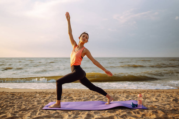 Yoga in the morning. Young woman in sportswear doing fitness exercise on the beach. Calmness and balance, a healthy lifestyle. - 写真・画像