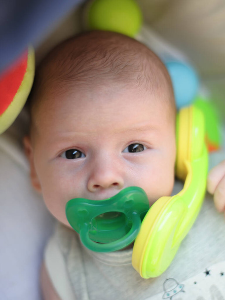 Funny baby boy is talking and using the toy telephone headset in carriage, with many colorful plastic toy and rattle around head. Close-up detail portrait. Love and family emotion - Фото, зображення