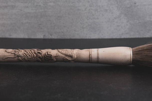 Chinese hand carved bone paintbrush on grey and black background. High quality photo - Foto, afbeelding