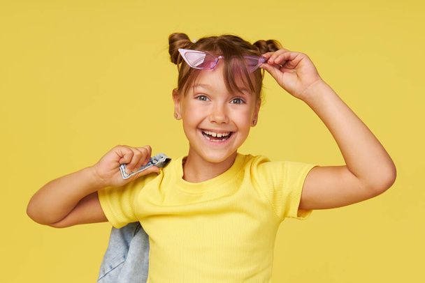 Portrait of surprised cute little toddler girl in the heart shape sunglasses. Child with open mouth having fun isolated over pink background. Looking at camera. Wow funny face - Foto, imagen