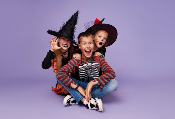 Funny children in carnival costumes in honor of Halloween on a purple background. - Fotoğraf, Görsel