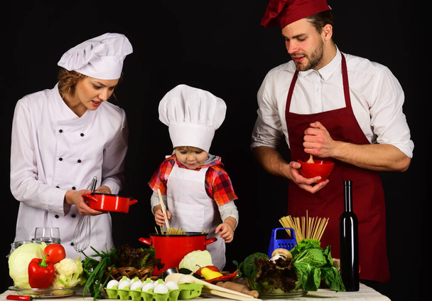 Child with parents cooking at kitchen. Happy family in chef uniform preparing dinner together - Foto, Bild