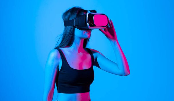Young woman in a black t-shirt using the VR goggles and communicating with friends in a metaverse social network. Future technology concept - Zdjęcie, obraz