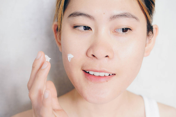 Portrait shot of young happiness Asian woman applying moisturizer cream on her face. Conceptual of beauty and skin care. - 写真・画像
