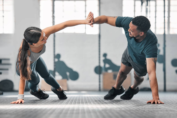 Healthy, fit and active gym partners exercising together as a couple, doing pushups and a high five. Boyfriend and girlfriend training and exercising in a health club as part of their workout routine. - Фото, изображение