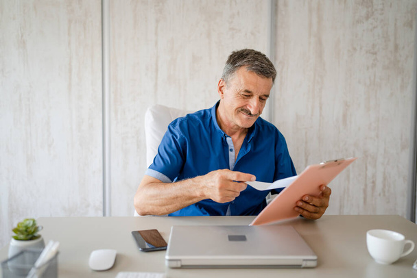 one senior man male caucasian entrepreneur or businessman checking documents or contract or report while sitting at the table desk in the office alone happy confident real people copy space - Photo, image