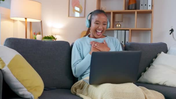 Woman having a funny conversation on an online video call with family, talking using headphones and a laptop. Laughing African American lady chatting on social media sitting on a sofa - 映像、動画