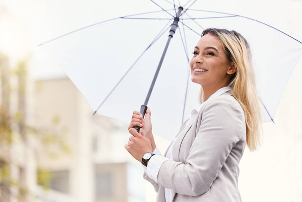 Insurance is her game. an attractive young businesswoman walking through the city with an umbrella - Photo, image