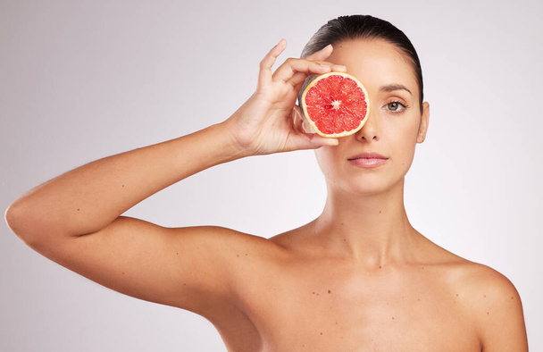 Wat is een huidverzorgingsroutine zonder vitamine c. een aantrekkelijke jonge vrouw die een grapefruit tegen een studioachtergrond houdt - Foto, afbeelding